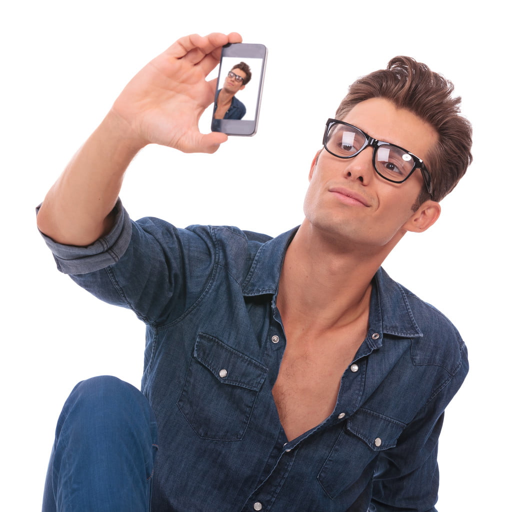 casual young man sitting on the floor and taking a picture of himself with his phone. isolated on white